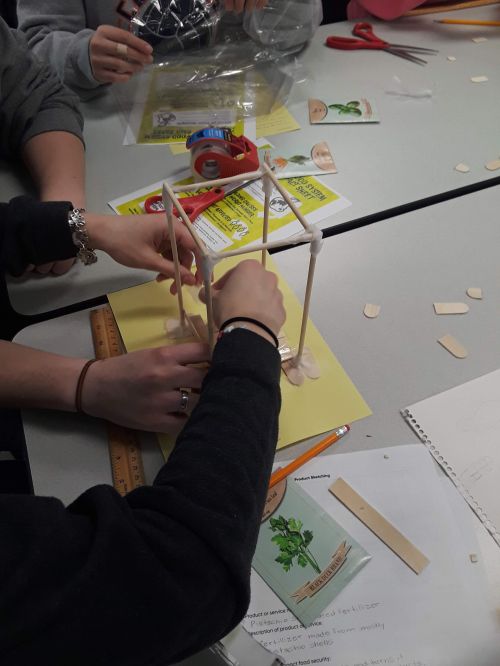 Hands putting together a structure made of sticks and tape.