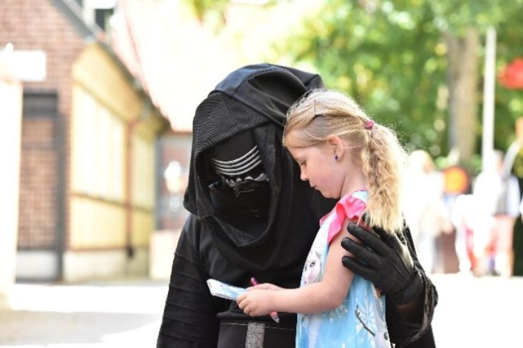 A young child holding up a paper and pencil to a character in costume.