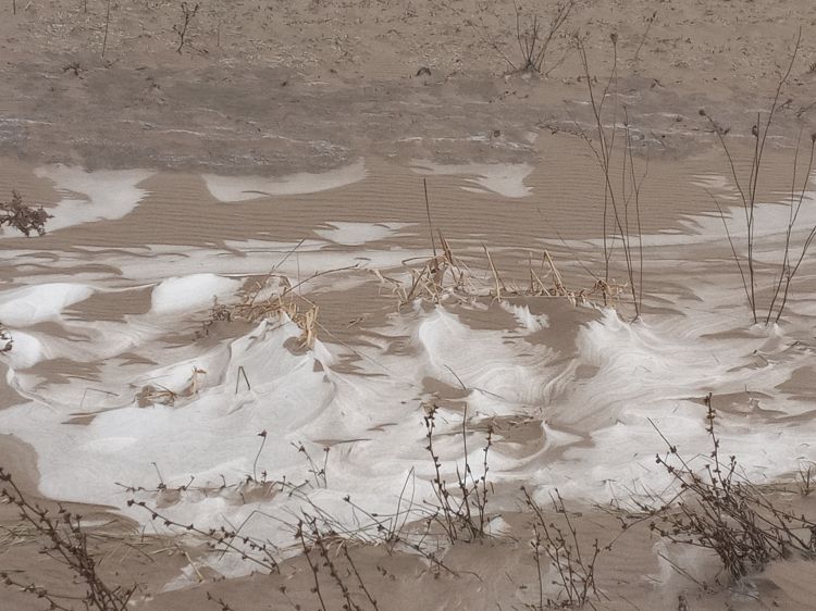 Snow drifts streaked with brown soil form rippled patterns across the ground, illustrating “snirt,” a mix of snow and windblown dirt from erosion.