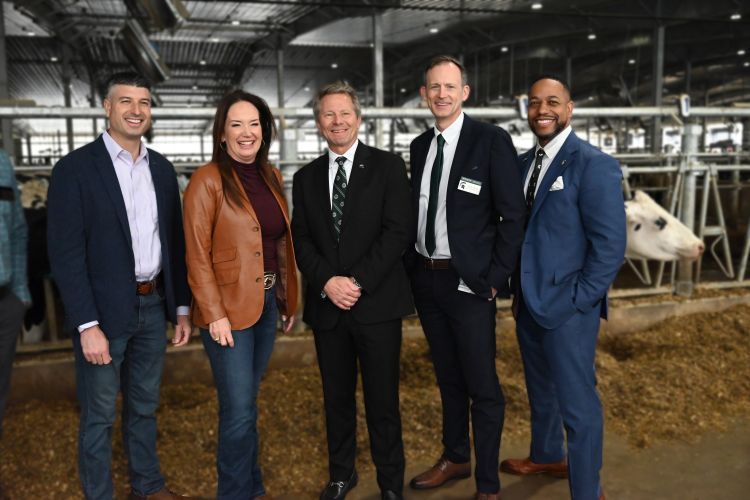five people posing for a photo in front of a line of cows eating at a bunk