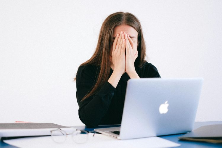 A woman holding her face while sitting in front of a computer.