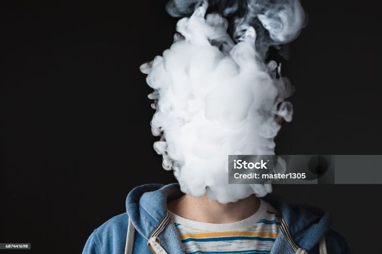 The face of vaping young man on black studio background