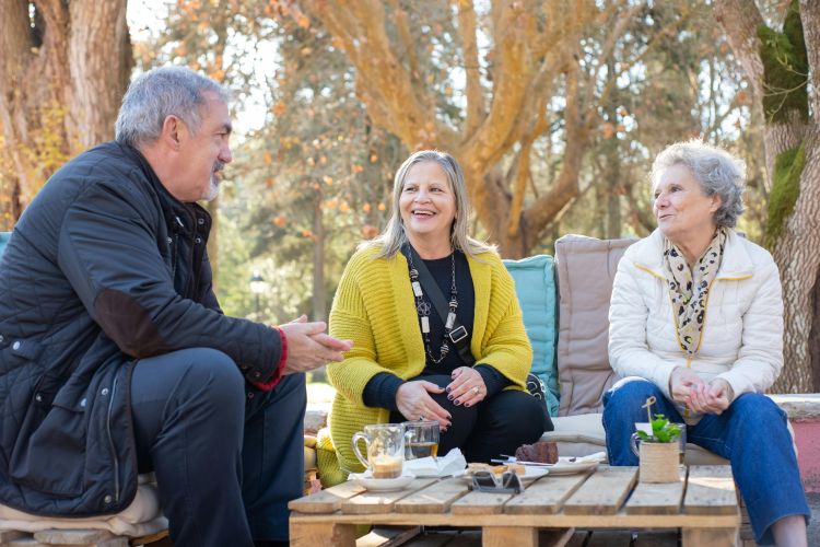 Three older adults sitting outside around a table drinking tea and talking.