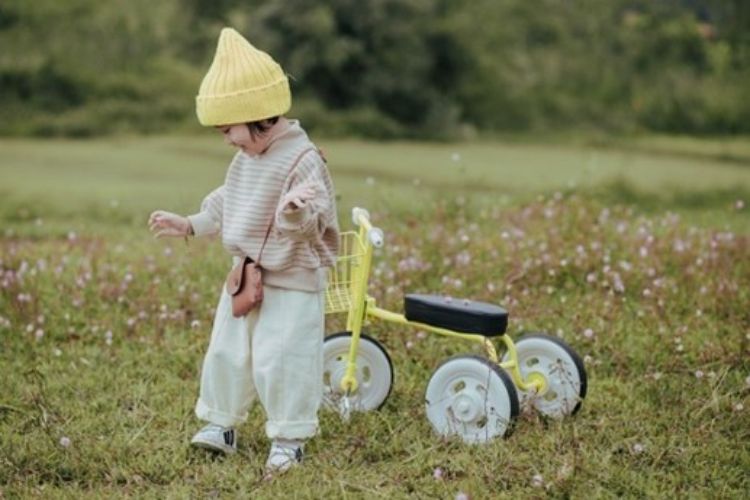 A child outside next to a tricycle.