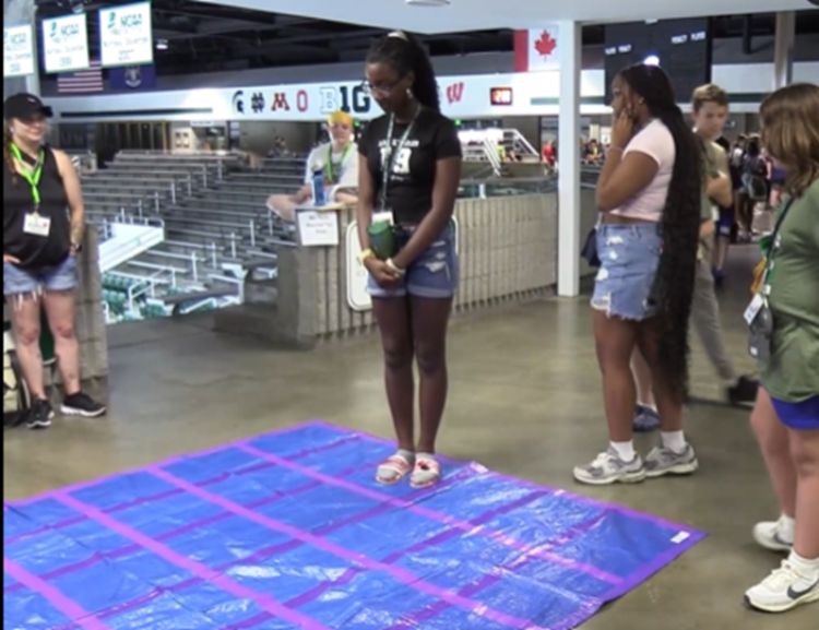 A girl standing on a tarp with a grid made out of duct tape.