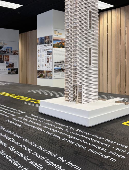 A wooden mockup of a building on display in an exhibit space.