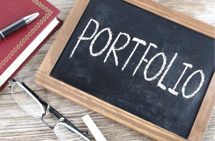Black chalkboard with the word Portfolio on it. Nearby are a pen, book and pair of glasses.