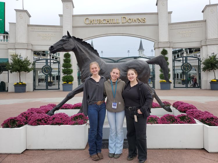 Three girls standing in front of a horse statue.