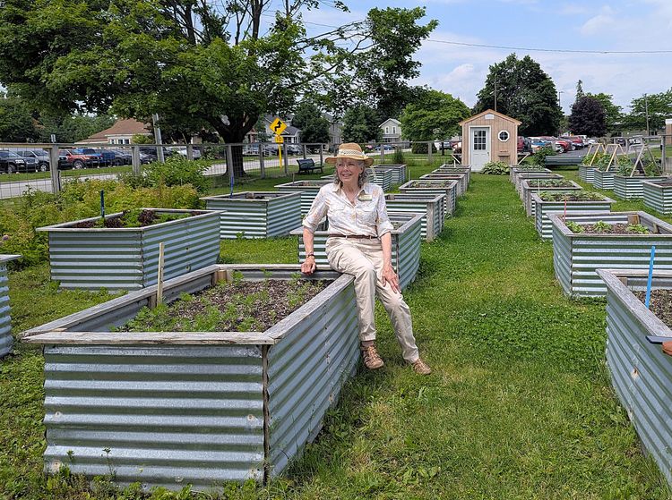 Catherine Stedman sits beside a raised garden bed at the Veggie Cart project, surrounded by rows of raised beds.