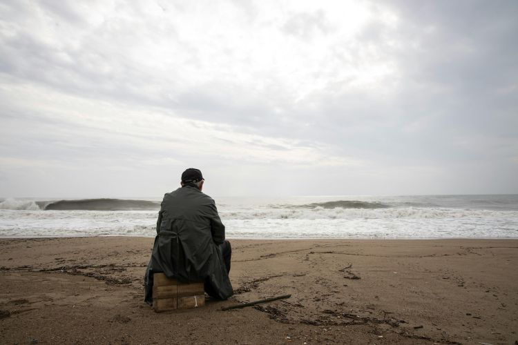 Man sitting alone on a pebbled beach.