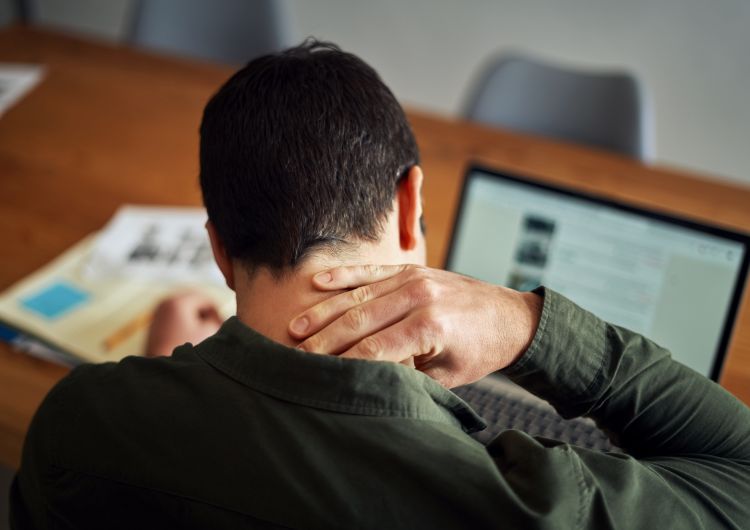 A man holds his neck while looking over a laptop screen.