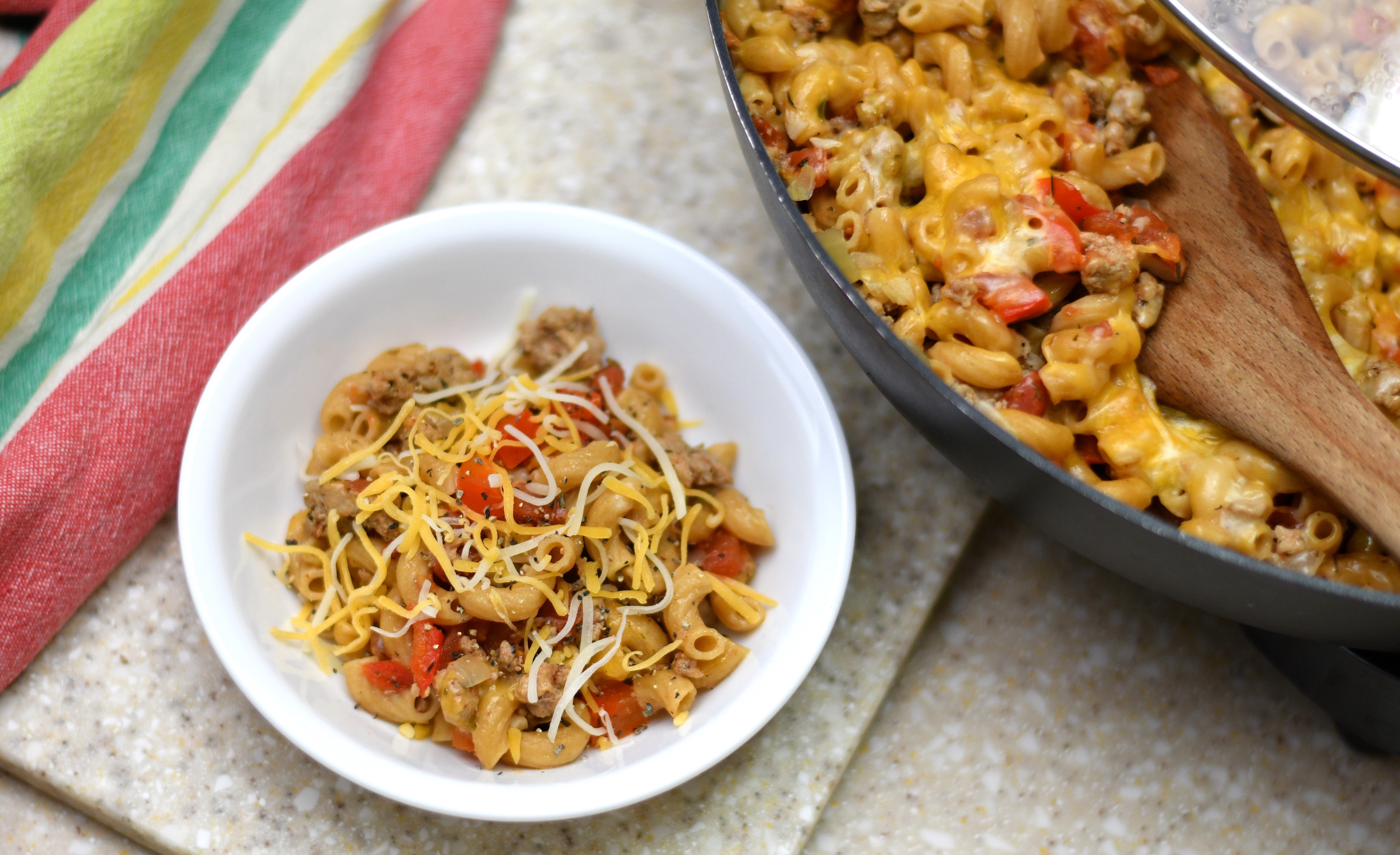 A photo of a bowl of pasta with tomatoes and meat next to a pan of food with a wooden spoon