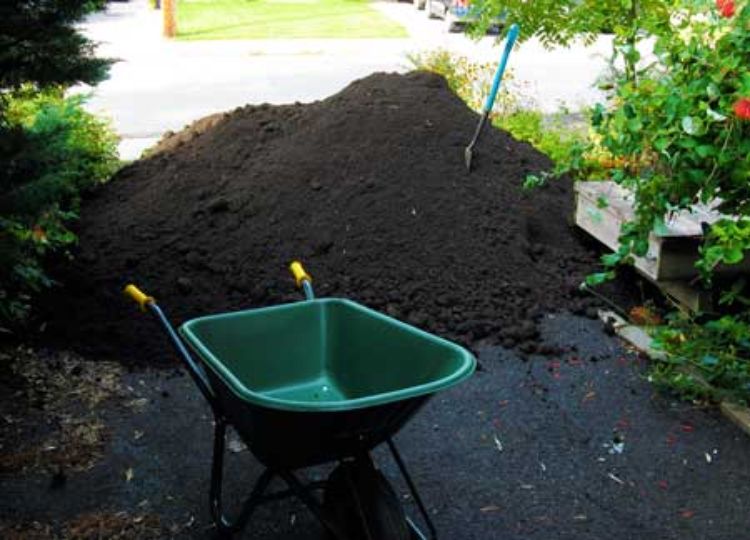 A pile of topsoil and a wheel barrow in a driveway.