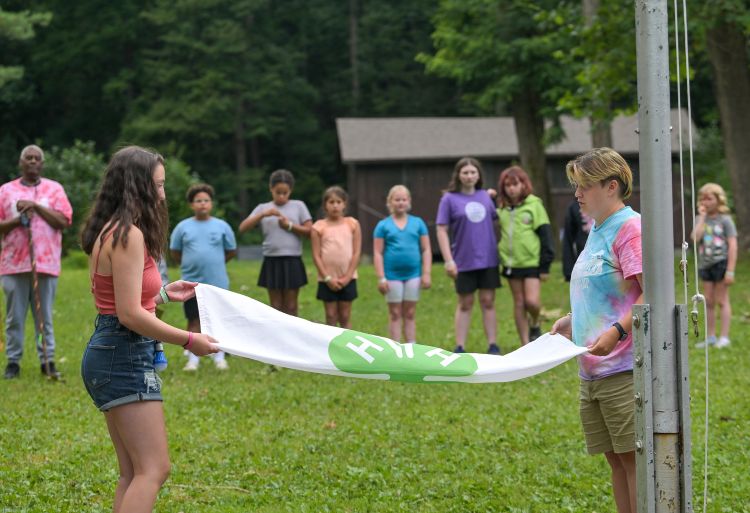 Youth folding a 4-H flag in an outdoor setting. Youth in the background.