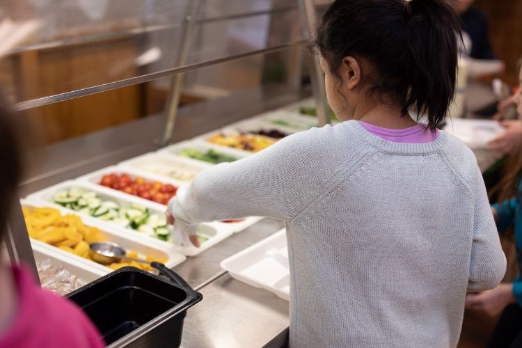 A student chooses cucumbers from the school salad bar.