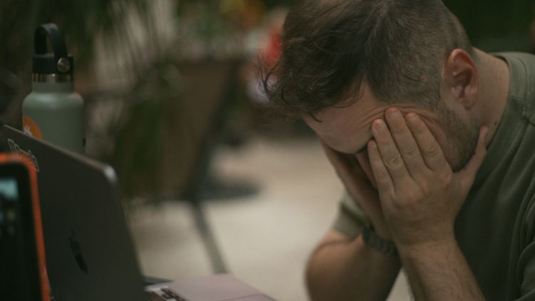A man deals with his stress by holding onto his face with both hands.