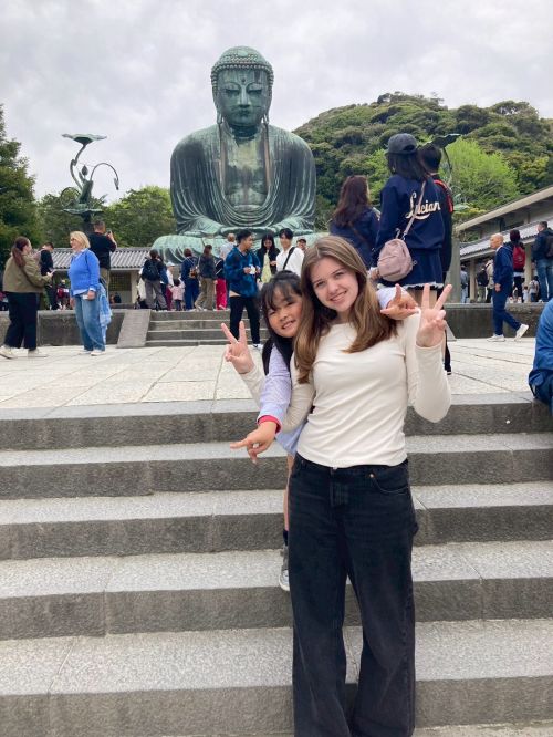 Two girls in front of a statue giving the peace sign.