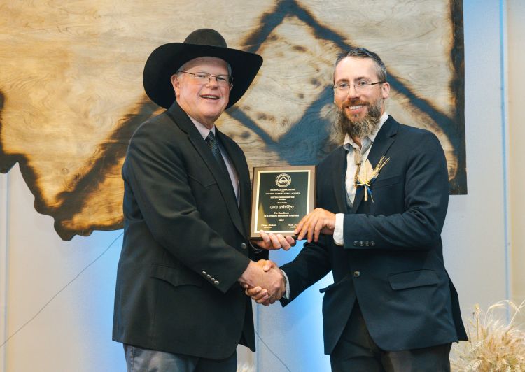Ben Phillips and NACAA President Scott Jensen shaking hands and holding a Distinguished Service Award plaque.