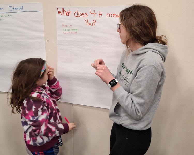 A teen girl and a young girl standing next to a flip chart that says 