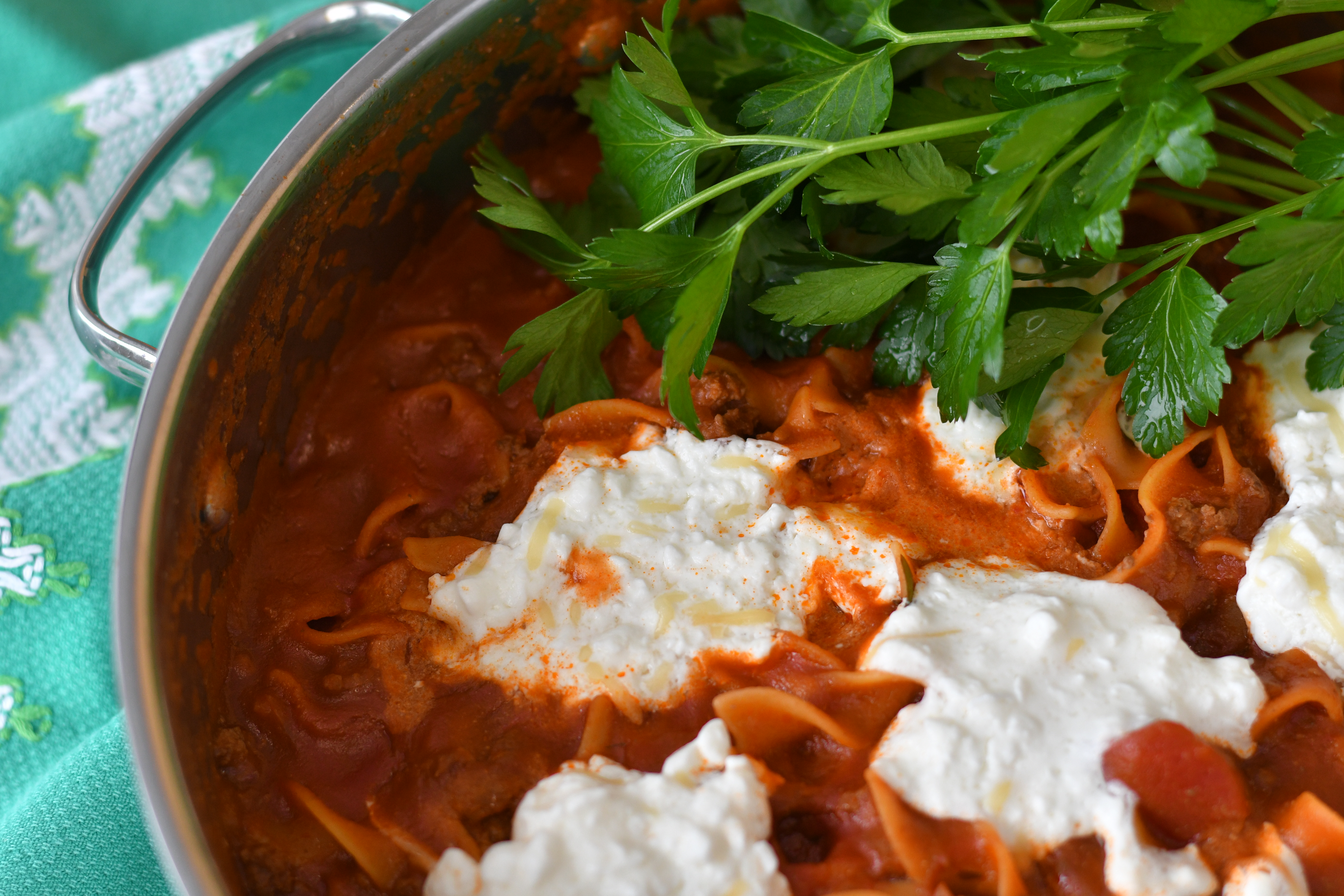 A photo of a pot of pasta with sauce and parsley