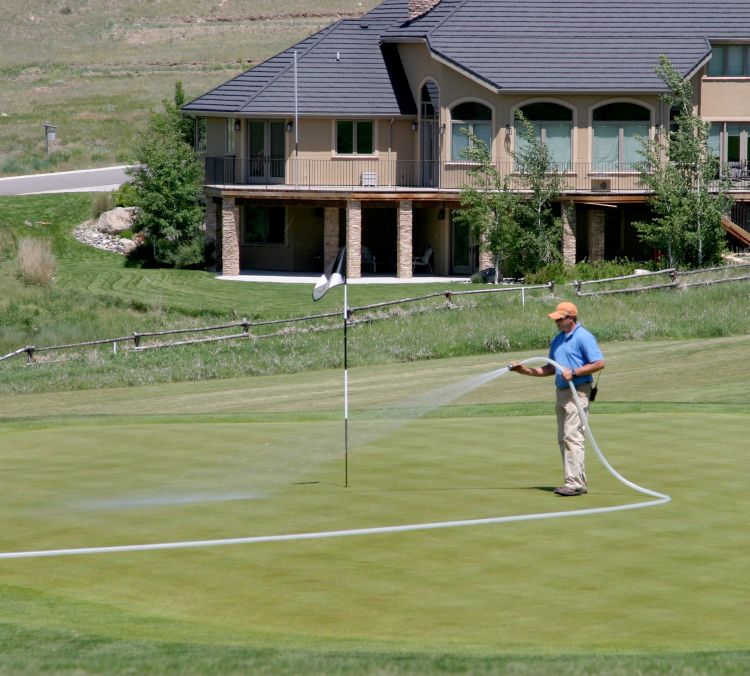 A man waters down a putting green on a golf course with a hose.