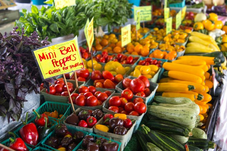 An image of colorful fresh produce at a farmers market, including peppers and tomatoes.