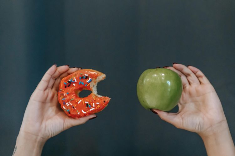 A person holding an apple and a donut.