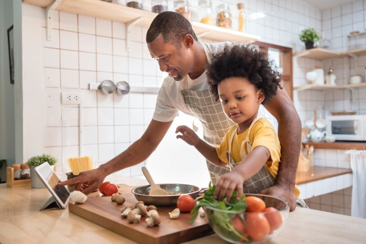 A parent and young child work together to make a meal in the kitchen.