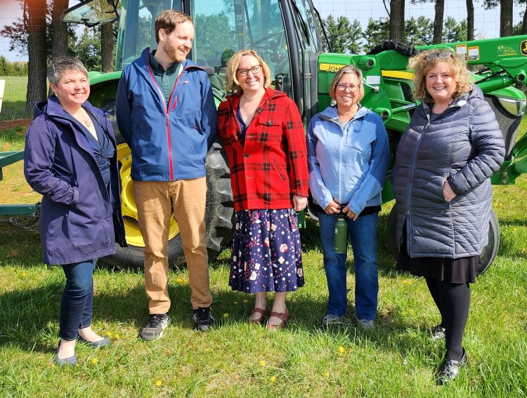 A photo featuring smiling people in front of a tractor.