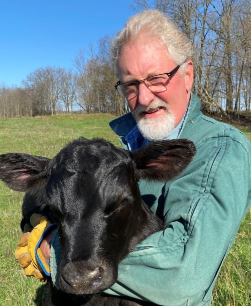 Mike VandeHaar posing for the camera in a green coat, holding a black-colored calf