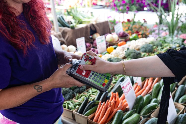 A person uses their WIC card to make a purchase at a farmers market.