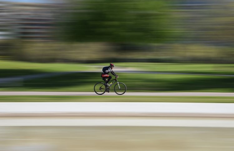 A photo of a bicyclist traveling quickly down the road, with the background blurred.