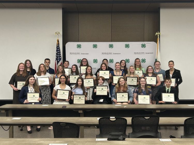 A group of youth holding up plaques in front of a 4-H backdrop.