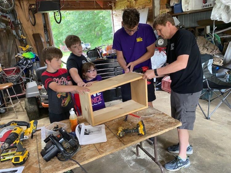 Four youth with an adult volunteer in a shop setting working on a wood project with tools.