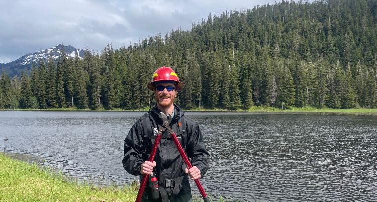 MSU Forestry student Harrison Remelts posing for a picture with a river, trees, and mountains in the background.