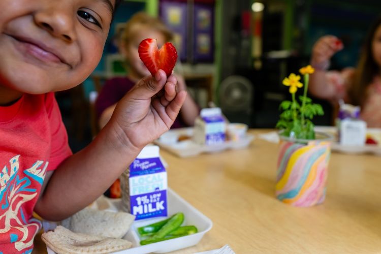 A child holds up a strawberry in the shape of a heart