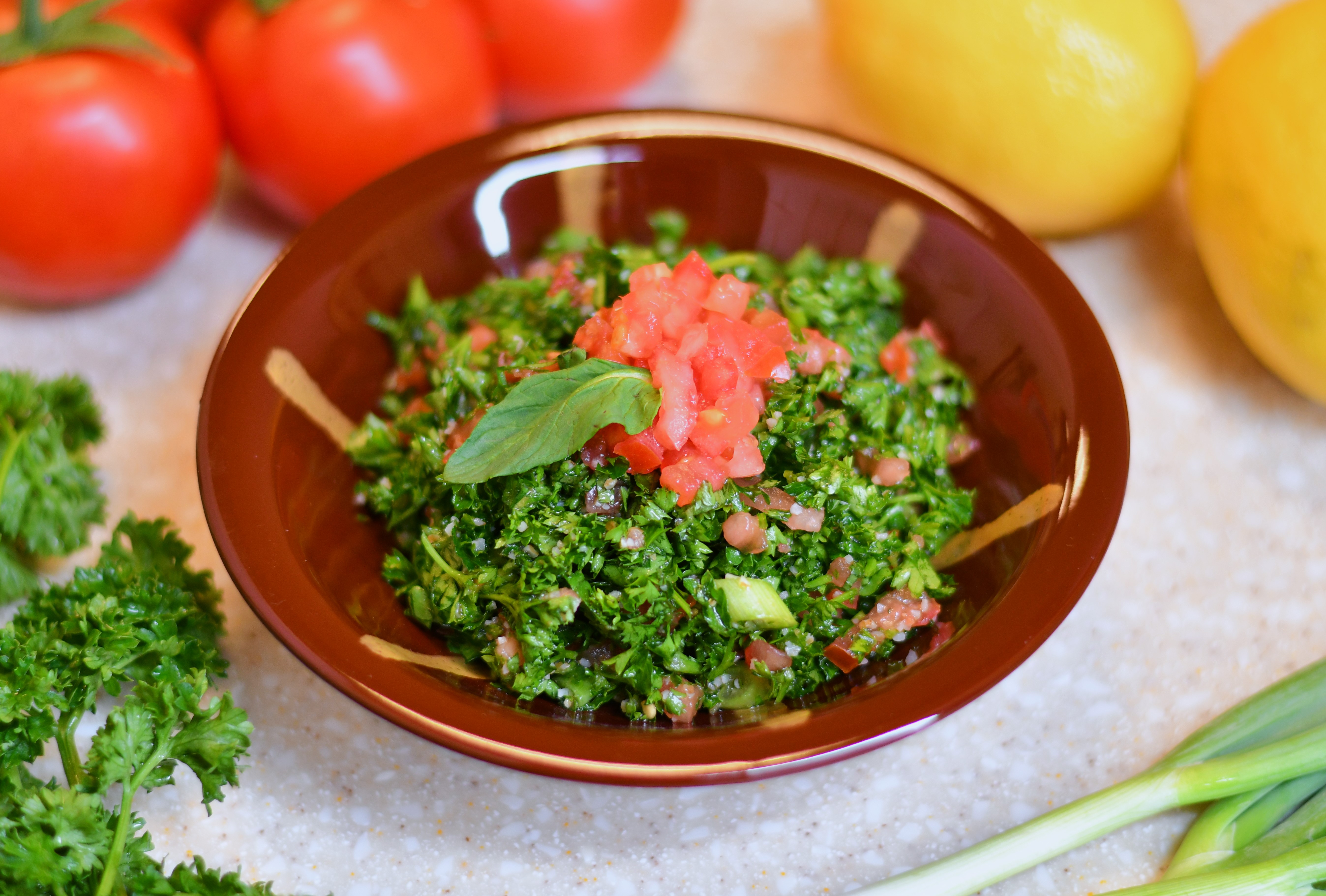A photo of a small bowl of a parsley tomato mixture topped with diced tomatoes and a mint leaf