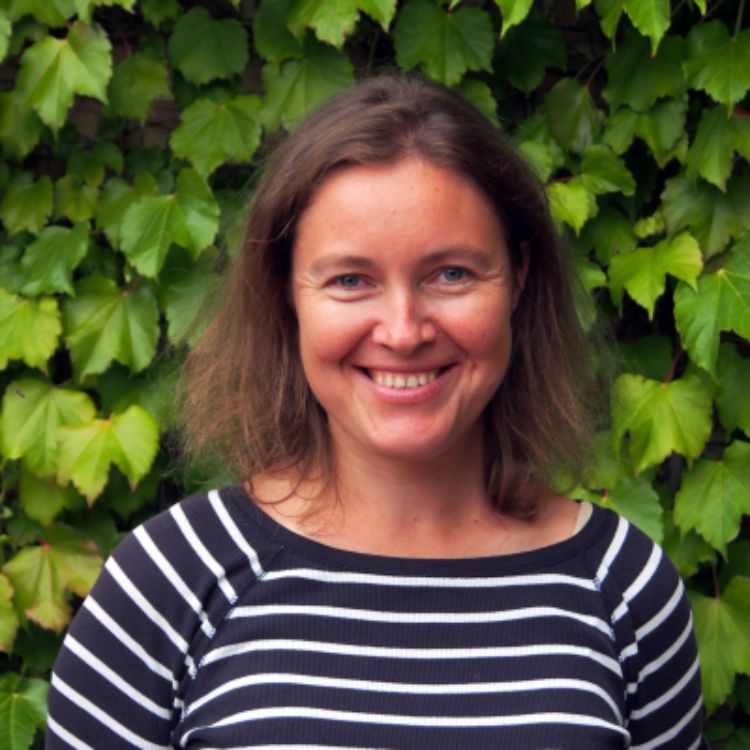 A headshot of Tanya Iretskaia smiling in front of a leafy backdrop