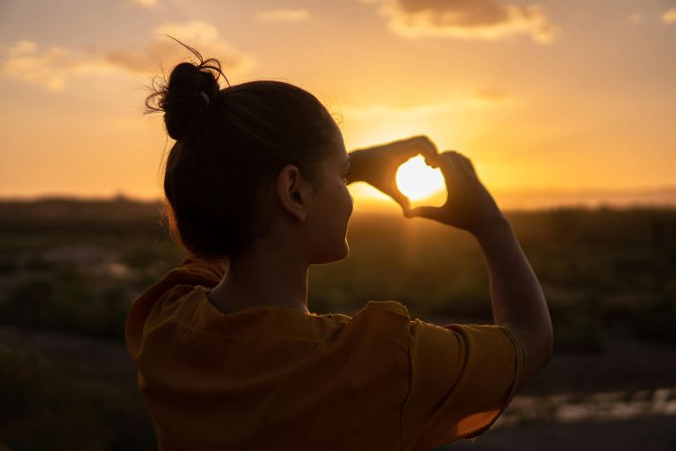 A woman at a sunset making a heart with her hands.