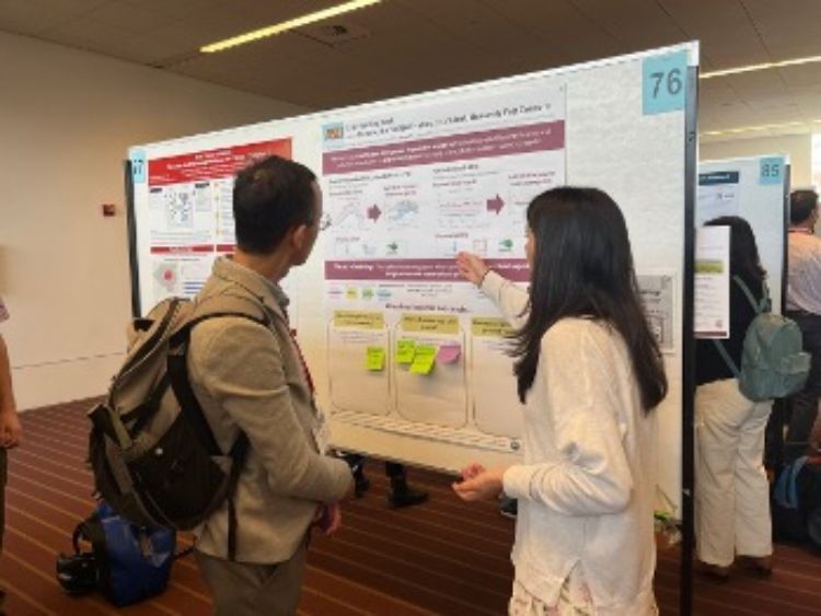 Photograph of two people discussing a research poster at a conference, with one person pointing to specific sections on the poster.