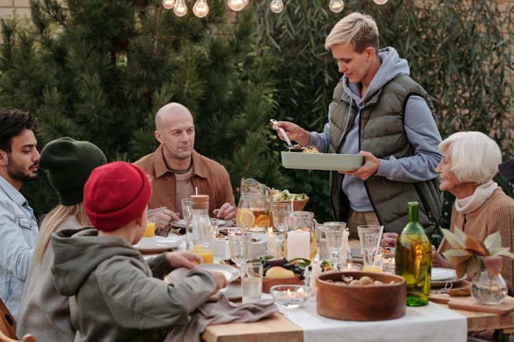 A multi-generational family gathering around an outdoor table to eat dinner.