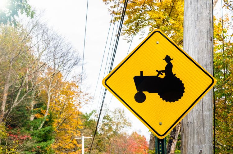 A yellow traffic sign of a farmer on a tractor with trees in the background.