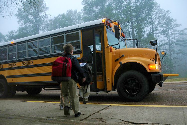 A child standing outside a yellow school bus.