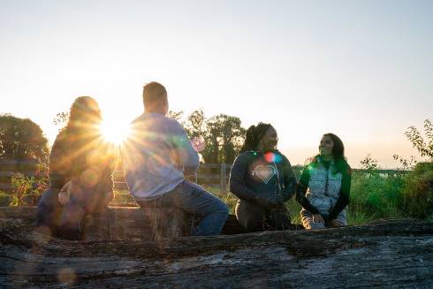 group of 4 youth sitting outside at sunset socializing and talking with eachother