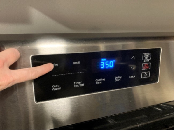 Close-up of an oven control panel with a hand pressing the 