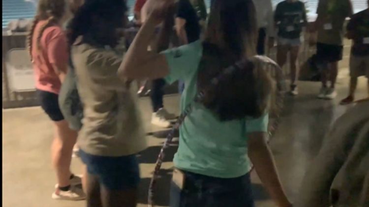 A group of youth in a circle holding hands through a hula hoop.