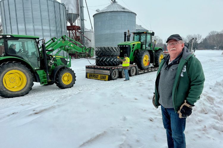 Image of Duane Stuever standing in front of his farm and a tractor in the background.