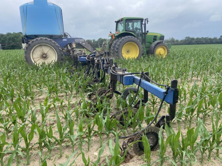 green tractor spreading fertilizer on a green field with a blue fertilizer sprayer