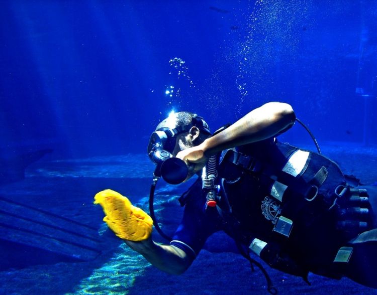 A person in a wet suite and scuba gear with a rag cleaning the inside of a tank.