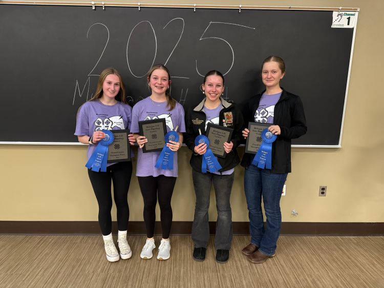 Four young ladies in purple shirts holding up blue ribbons and plaques.